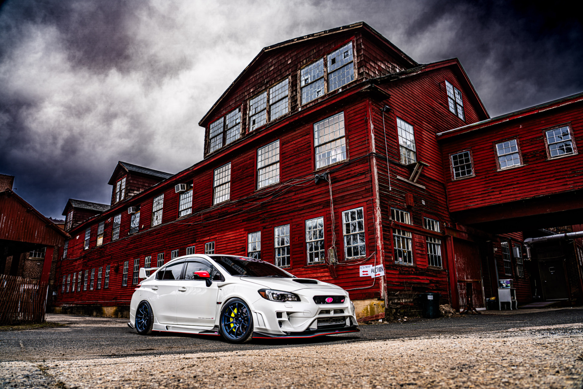 White Subaru STI parked in front of a historic red factory building