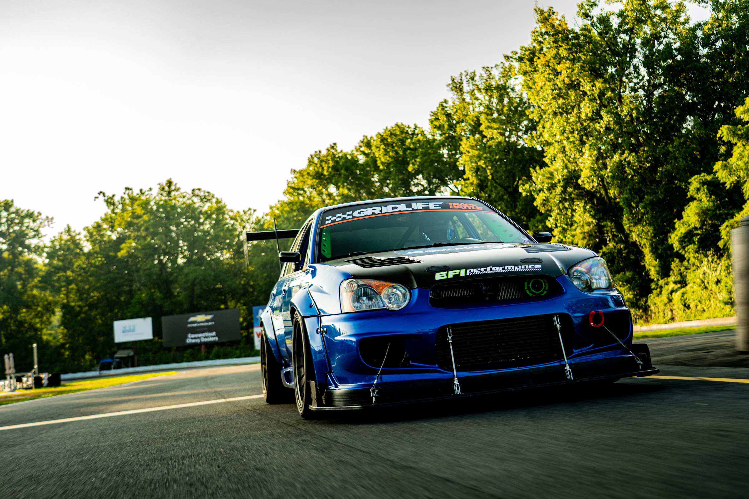 Blue widebody STI rolling shot along the treeline