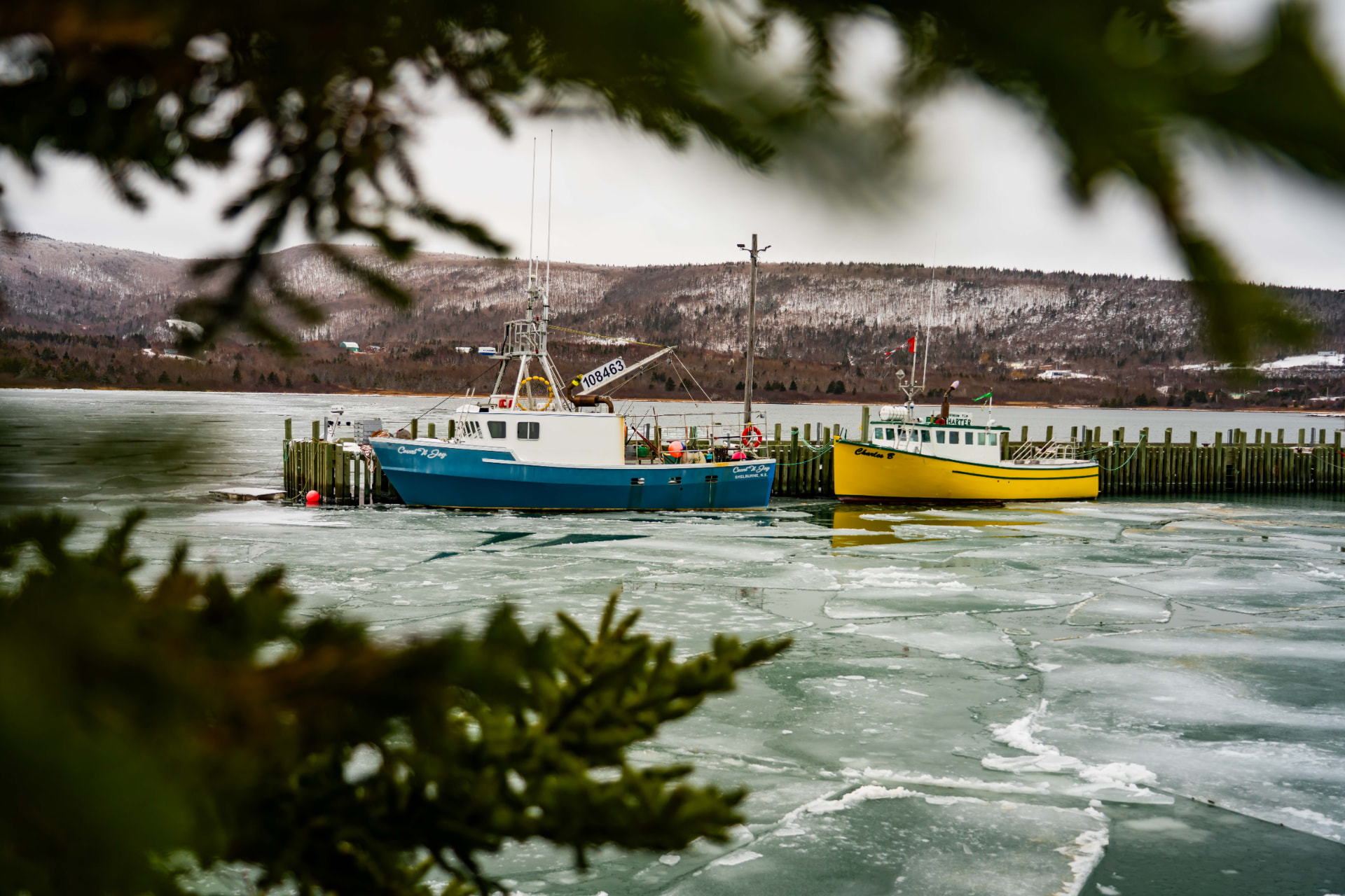Colorful fishing boats docked along a icy shoreline with snow-covered hills