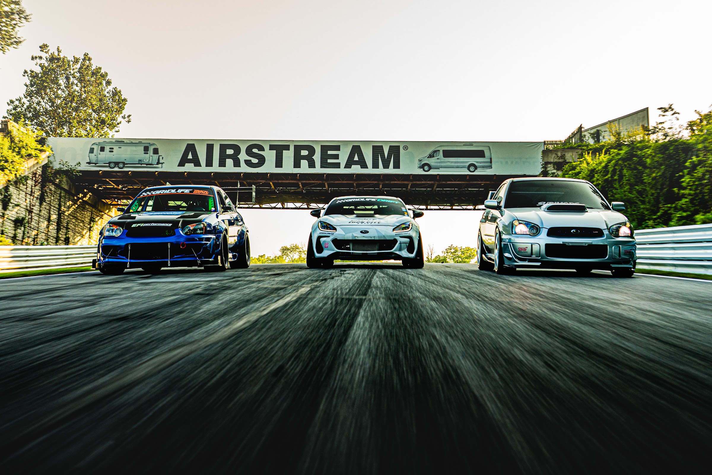 Blue widebody STI rolling shot on a wooded road