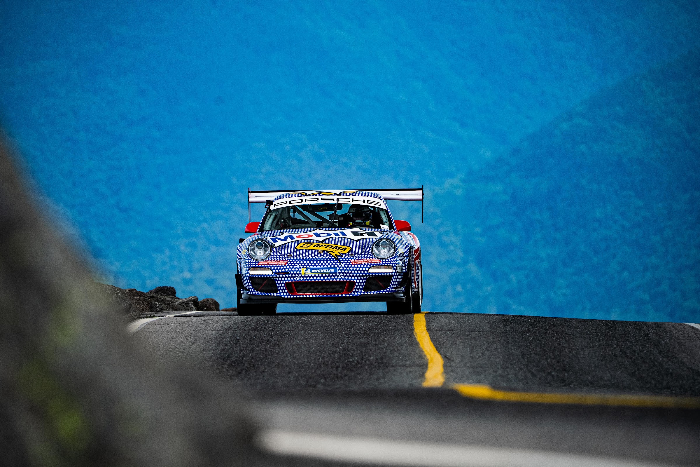 Livery-wrapped race car apexing under blue skies